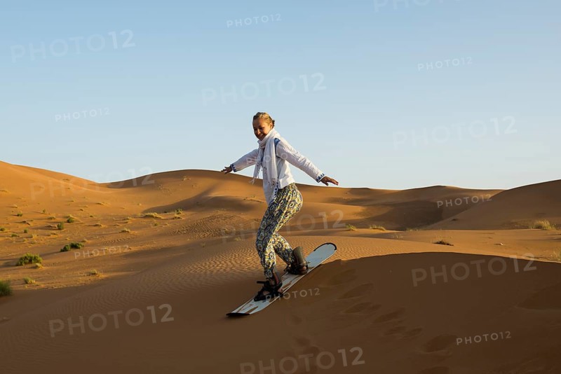 Young woman with snowboard in the sand dunes, near Merzouga, Meknès-Tafilalet region, Erg Chebbi, northern Sahara, Morocco