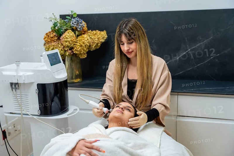 Woman undergoing a professional facial rejuvenation treatment performed by a cosmetologist using an advanced beauty device at a modern aesthetic clinic for skin care and wellness