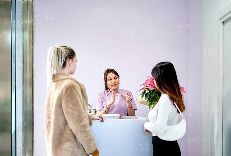 At a busy beauty salon, a staff member warmly engages with clients at the reception desk. The atmosphere is professional, inviting, and focused on customer satisfaction