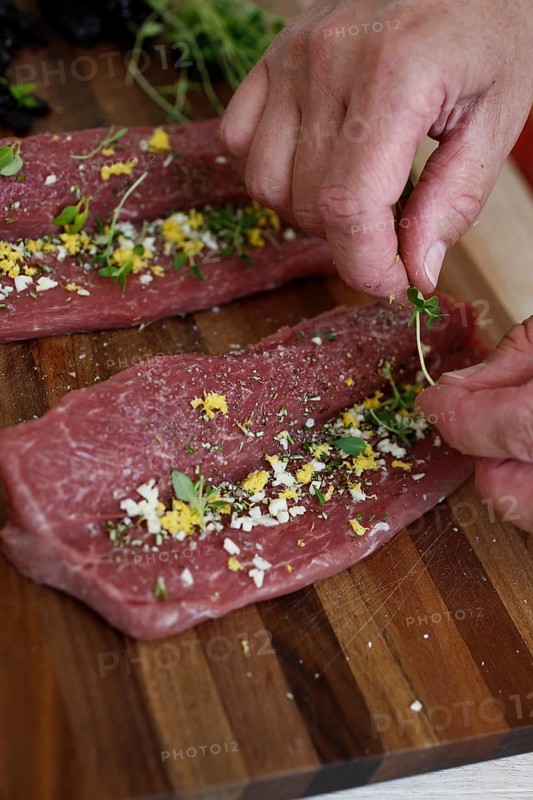 Swabian cuisine, preparation of lamb with prunes, raw lamb stuffed with herbs, rosemary, sliced garlic, lemon zest, fillets on wooden board, grandmother's cooking, regional, home cooking, typical Swabian, traditional cuisine reinterpreted, food photography, men's hands, studio, Germany