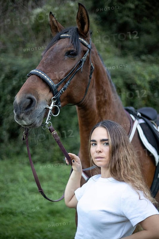 A young woman stands beside a horse in a tranquil outdoor setting. The close-up captures their connection, highlighting the beauty and trust between human and animal