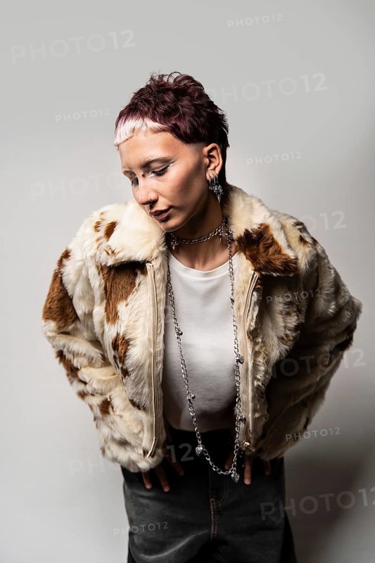 A woman strikes a pose in a stylish faux fur jacket, exuding confidence and boldness. The minimalist light grey backdrop enhances the edgy fashion statement