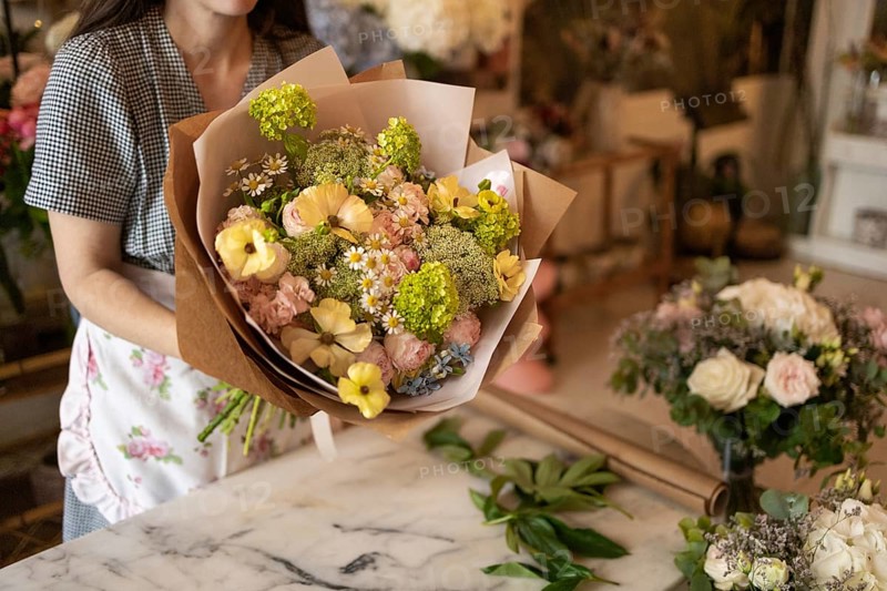 A woman holds a vibrant bouquet of flowers in a flower shop. The scene captures the lush variety of blooms and the creative atmosphere of the florist workspace