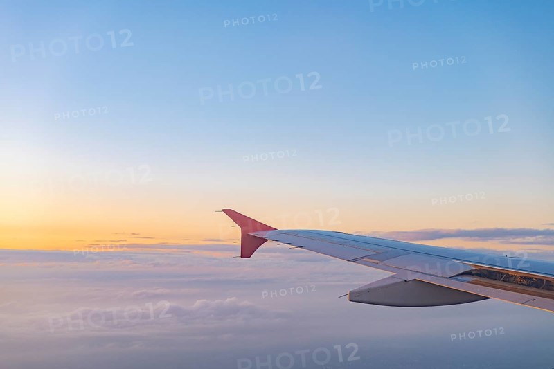 A stunning view from an airplane window capturing the wing against a colorful sunset sky, with clouds below. The gradient of colors creates a serene travel moment