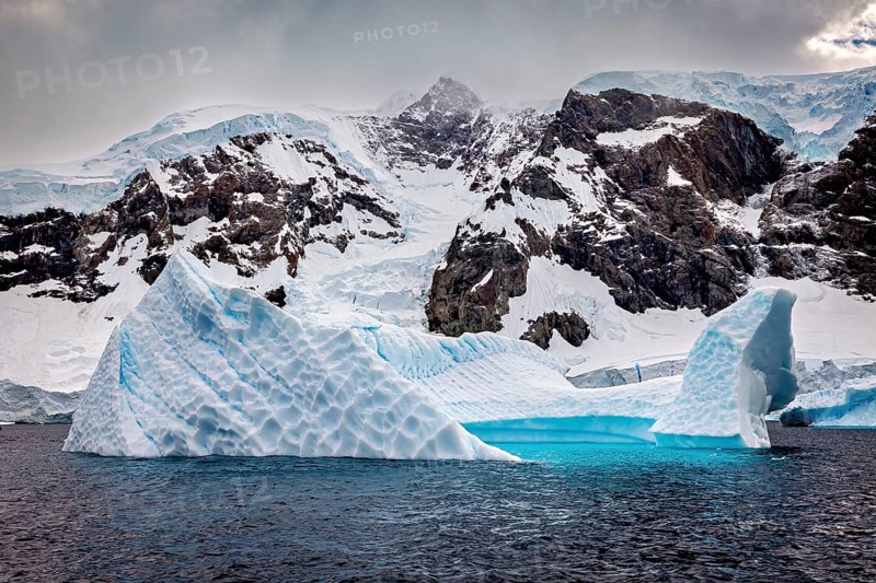 Icebergs with snow-covered mountains in the background under a dramatically darkening sky, icebergs in the Southern Ocean in Antarctica