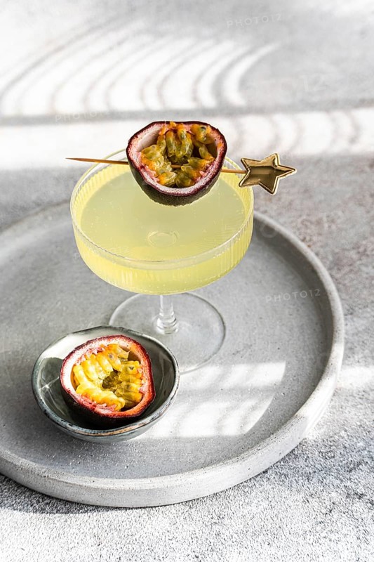 Elegant gin and tonic cocktail mixed with passion fruit juice, garnished with a fresh passion fruit half, presented on a stylish gray tray under soft lighting