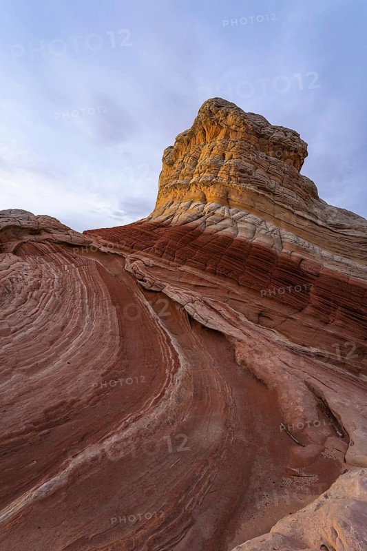 Expansive view of a unique sandstone rock formation under a clear sky at White Pocket, Arizona, showcasing swirling red and beige patterns