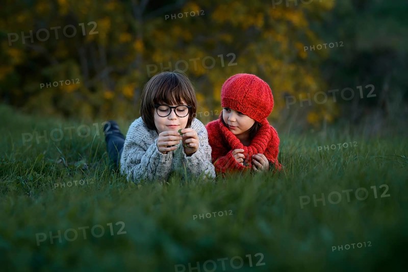 A young girl and boy, siblings, playfully engage outdoors, enjoying a crisp autumn day in a vibrant park setting
