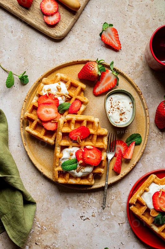 A cozy, rustic setting featuring homemade waffles topped with fresh strawberries and yoghurt. This sweet and romantic dessert is perfect for a delightful treat