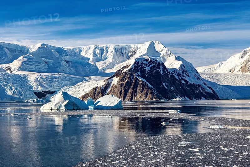 White, clear chunks of ice float in the calm sea in front of imposing white mountains, The landscape of Antarctica