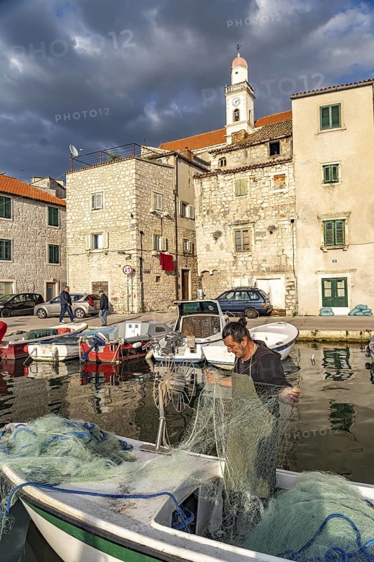 Fisherman with a net on his boat in the small harbour in the old town of Sibenik, Croatia