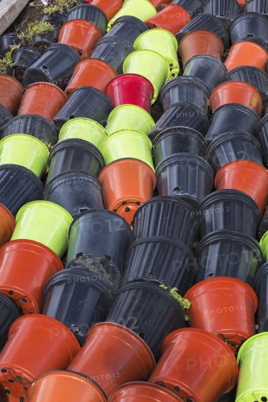 Rows of discarded tipped over red, black and lime green plastic containers on the ground with withered plants, Quebec, Canada