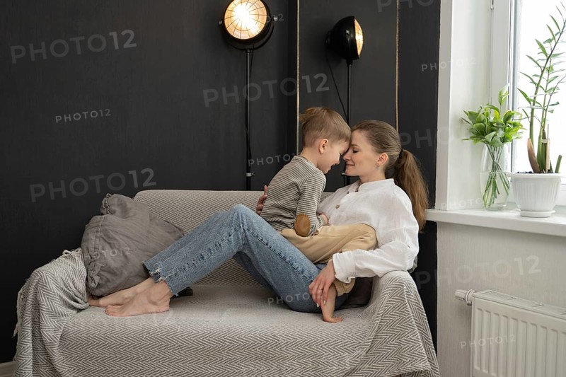 A mother and child share a tender moment, seated on a cozy couch. The room is warm ambiance is enhanced by soft lighting and minimalistic decor, promoting relaxation