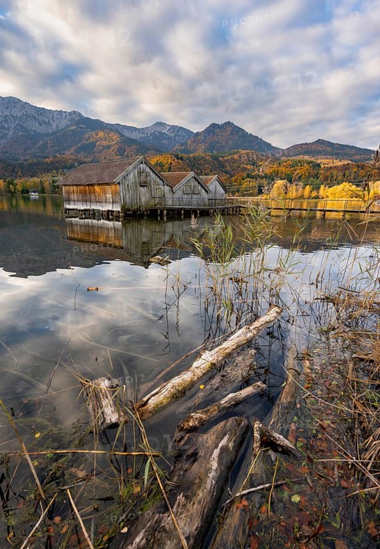 Boathouses in the lake at sunrise, Lake Kochel in autumn with reflection, behind mountain peaks Herzogstand and Heimgarten Upper Bavaria, Bavaria, Germany