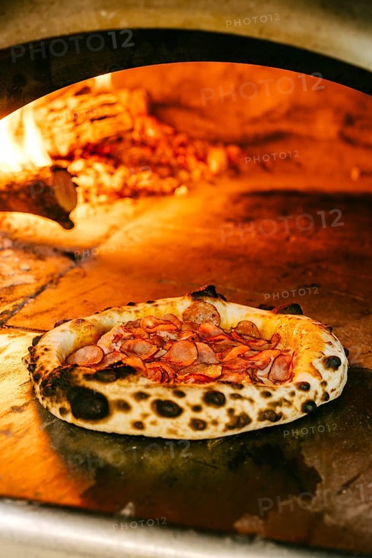 Freshly baked wood-fired pizza topped with smoked pork, salami, pork sausages, chicken fillet, mozzarella, and tomato sauce. Crispy crust with a golden char from the open flame