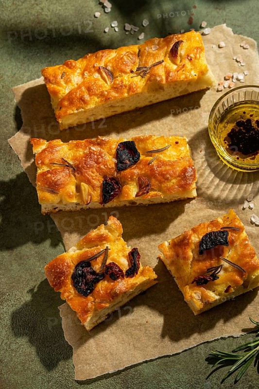Warm, golden homemade focaccia bread topped with rosemary and garlic, served on parchment. Beside it, a dish of olive oil and balsamic vinegar for dipping. Perfect for Italian cuisine lovers