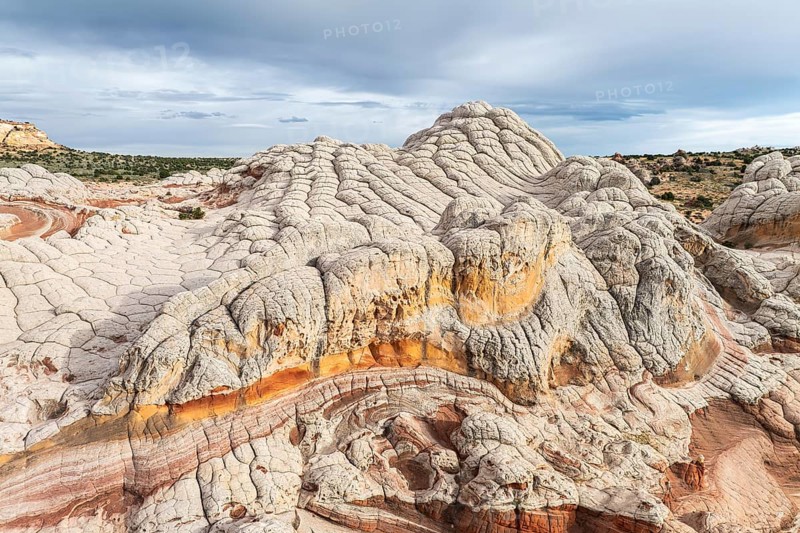 Panoramic view of the unique and colorful sandstone formations at White Pocket, Arizona, USA. Captured on a cloudy day, presenting undulating textures and vibrant earth tones contrasted against a dynamic sky