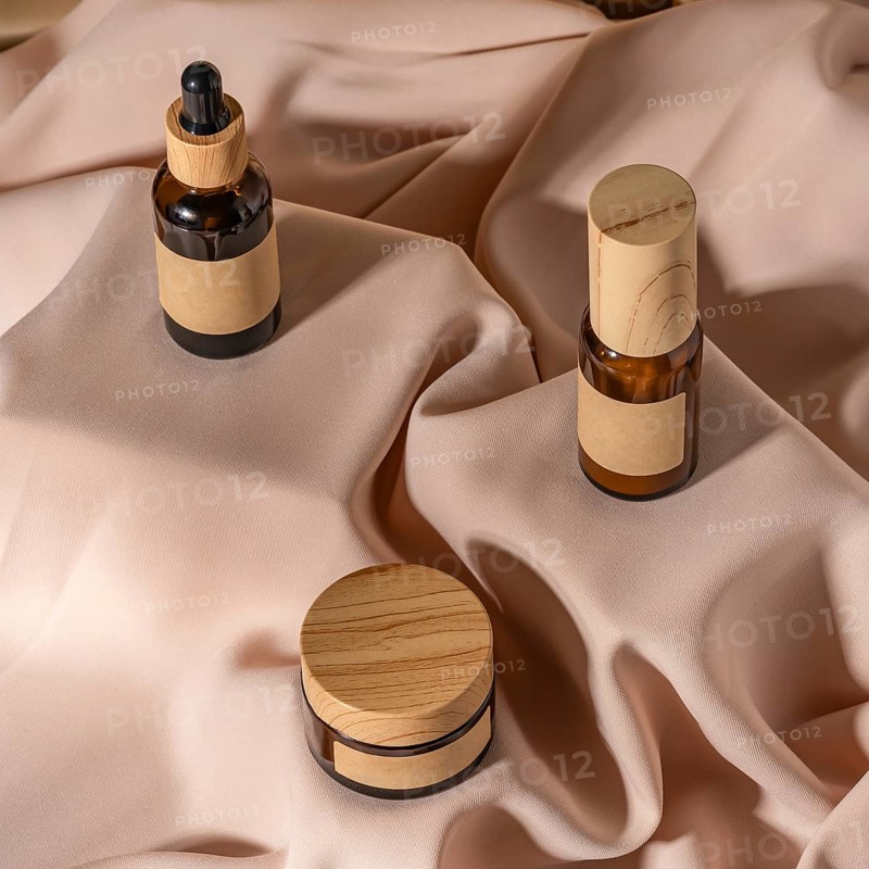 A collection of eco-friendly skincare products displayed on soft, beige fabric The set includes amber glass containers with wooden lids, accentuating a minimalist, natural aesthetic