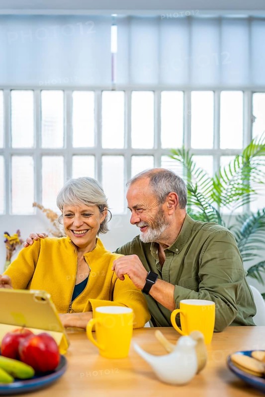 Vertical photo of a caucasian happy mature couple using digital tablet enjoying time together at home