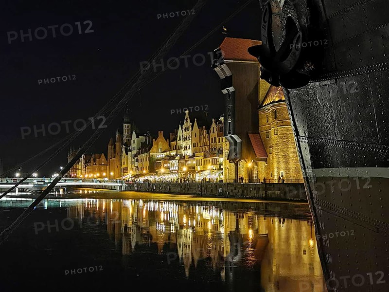 Night view of a ship's bow and illuminated historic buildings on the Motlawa River in Danzig, Poland