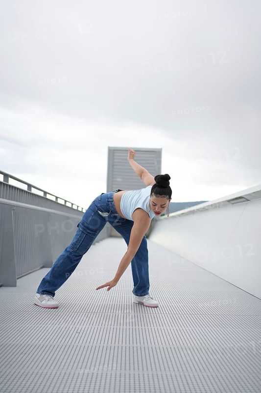 A woman is doing a dance on a white ledge. She is wearing blue jeans and a blue shirt