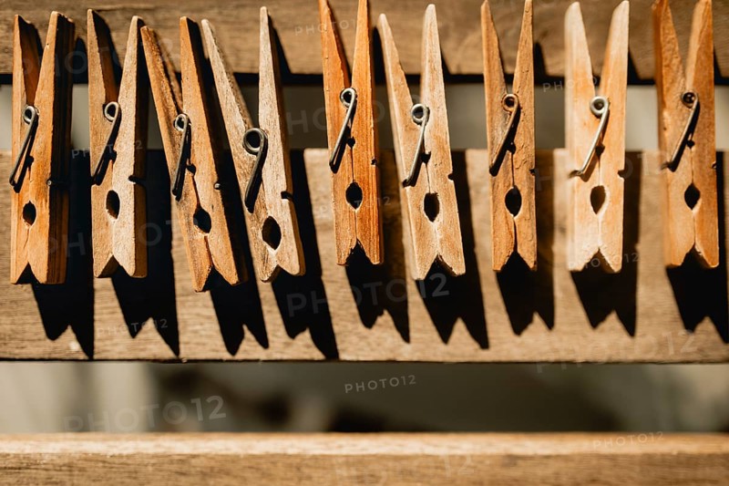 A row of wooden clothespins casting shadows on a rustic clothesline. The warm sunlight highlights their natural texture, evoking a sense of simplicity and nostalgia
