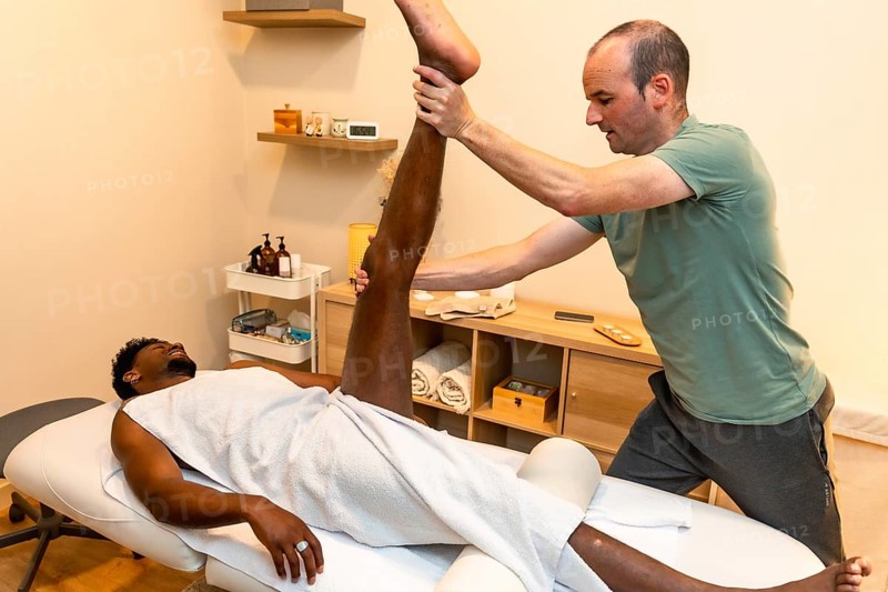 Physiotherapist performing a deep leg stretch on a male patient lying on a therapy table, focusing on physical therapy and rehabilitation exercises in a clinic setting