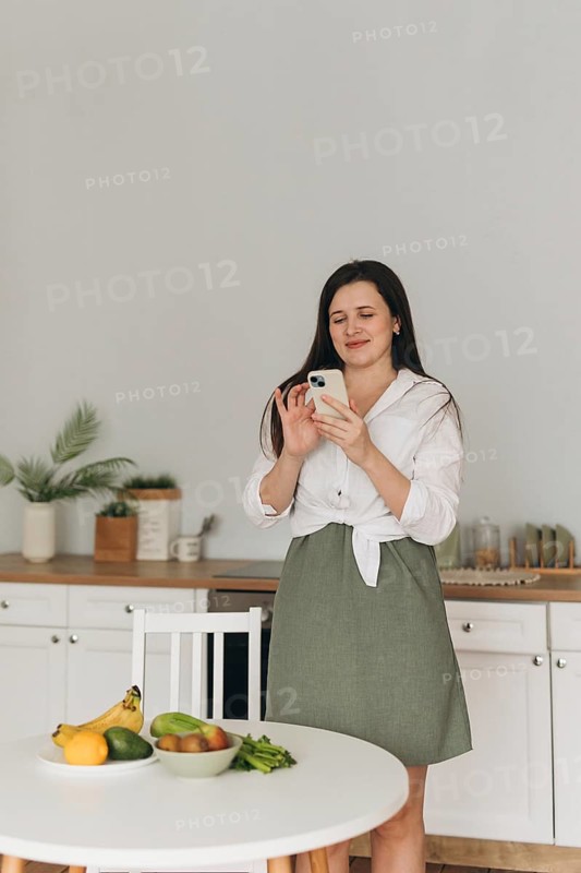 A nutritionist in a calming kitchen setting uses a smartphone for health advice, surrounded by a variety of fresh fruits and vegetables on a table
