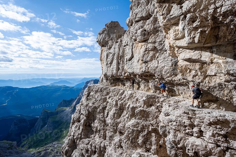 Three mountaineers on an exposed rock band in the secured via ferrata Bocciere Centrale, Brenta Mountains, Brenta-Adamello Natural Park, Trentino, Italy