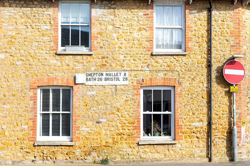 Vintage listed road distance mileplate sign historic old stone building, Fore Street, Castle Cary, Somerset, England, UK