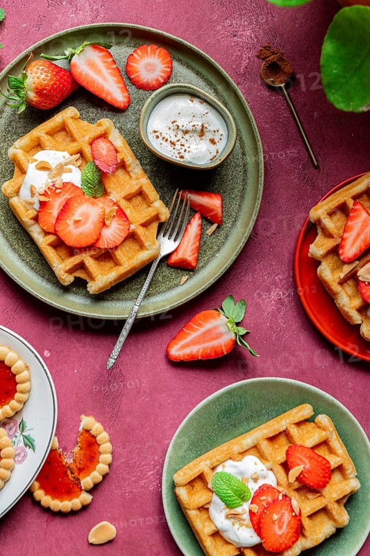 A rustic plate of homemade waffles garnished with fresh strawberries and yoghurt on a vibrant background, creating a romantic and sweet dessert setting