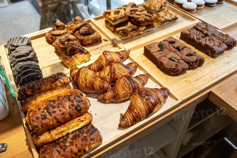 Assorted freshly baked pastriesgolden croissants, chocolate brownies, cinnamon rolls and fruit tartsneatly arranged on wooden trays at a modern bakery counter, ready to enjoy
