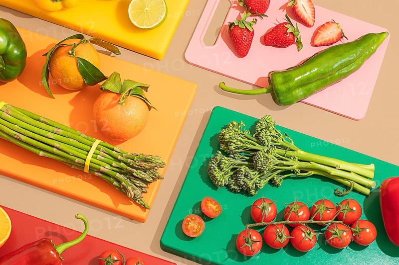 A vibrant display of fresh fruits and vegetables on multicolored cutting boards, featuring oranges, strawberries, asparagus, tomatoes, and more, creating a lively and healthy scene