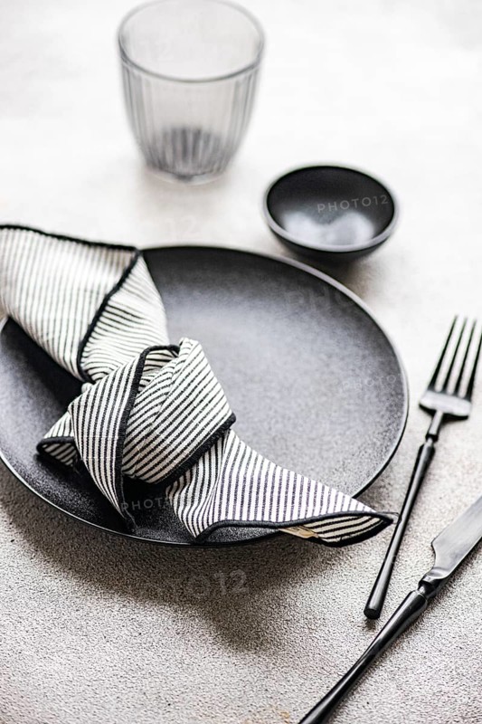 A stylish table setting featuring a black plate, black cutlery, and a striped napkin. The monochrome theme adds elegance and sophistication to any dining experience