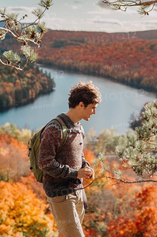 A person enjoys a peaceful hike in Quebec, Canada during autumn. The vibrant fall foliage surrounds a calm river, illustrating the season's natural beauty and tranquility