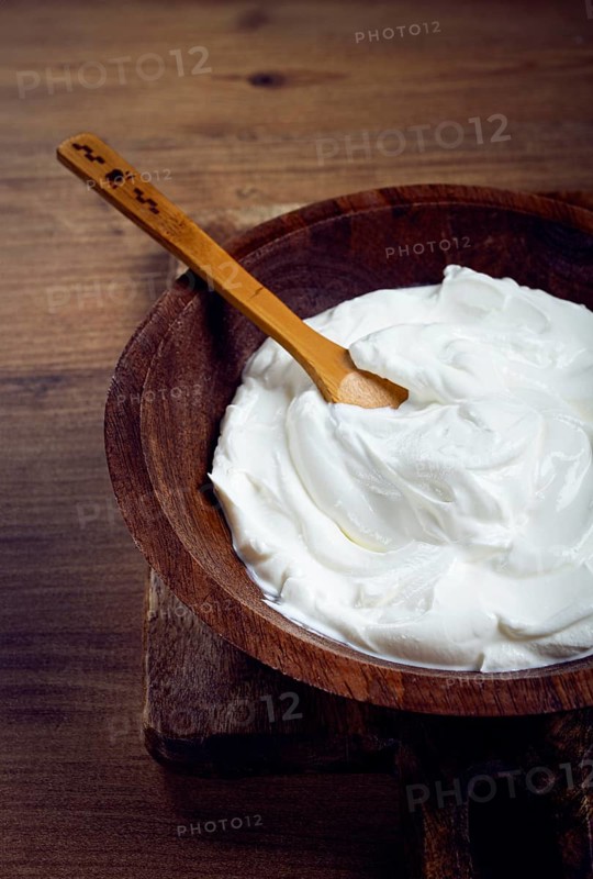 Sour cream in a wooden bowl, on a wooden table, top view, close-up, no people
