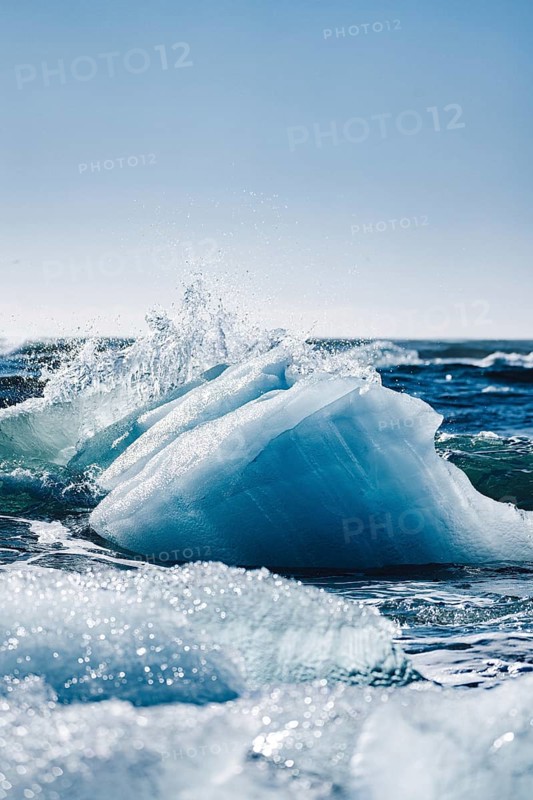 Sparkling ice formations glisten under the sun at Diamond Beach, Iceland, creating a stunning contrast with the deep blue ocean waves, showcasing nature's pristine beauty