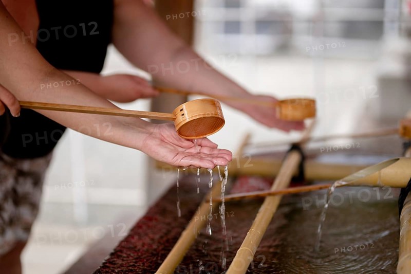 Close-up of people performing the traditional hand washing ritual at Shitenno-ji temple in Osaka, Japan, using wooden ladles to purify hands in clear water