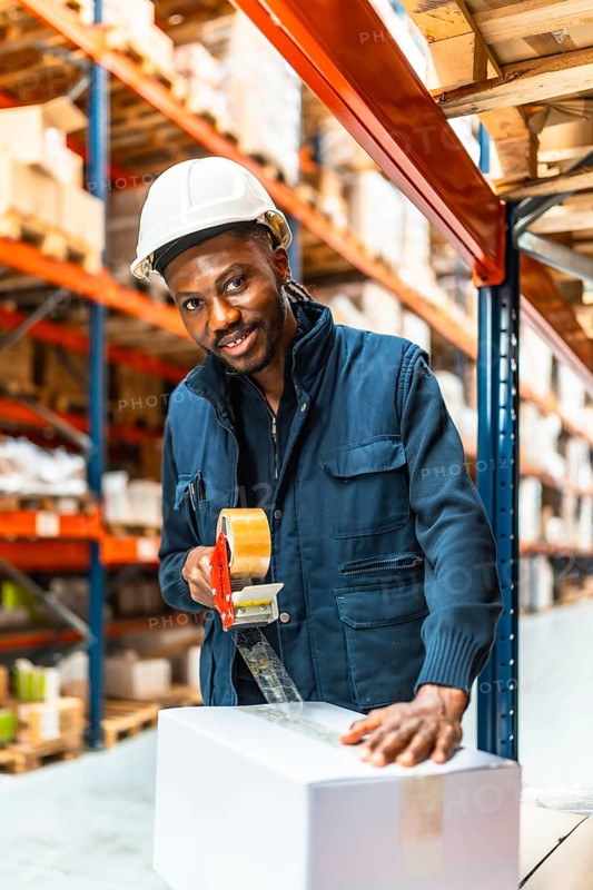 African smiling worker taping boxes closed before delivery in a shipping warehouse