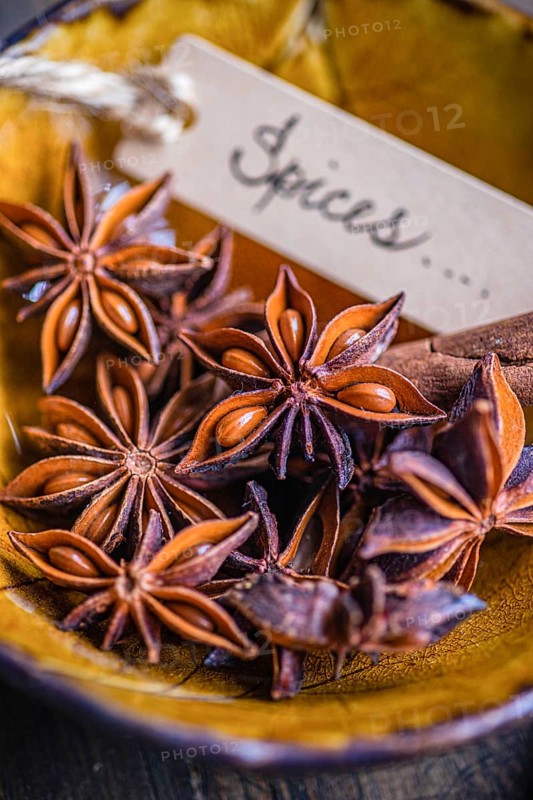A close-up view of star anise and cinnamon sticks arranged in a golden bowl, accompanied by a handwritten label reading Spices. The cozy ambiance highlights the vivid textures and rich colors of these aromatic ingredients