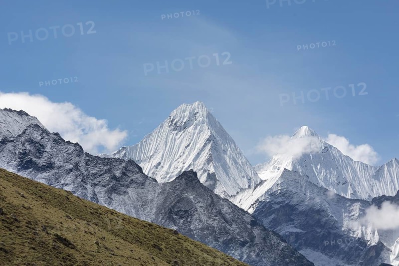The image captures the breathtaking view of Mount Everest, with its snow-capped peak reaching towards a clear blue sky, surrounded by rugged terrain and wispy clouds