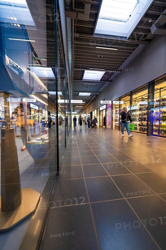 Interior view of a modern shopping centre with shops and people walking past, Outlet City Metzingen, Germany