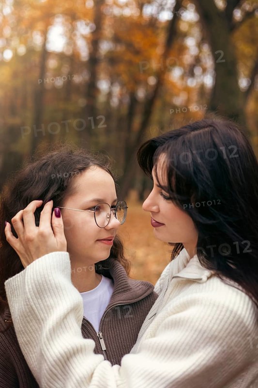 A tender moment between a mother and daughter, surrounded by warm autumn colors in a forest setting. The embrace captures the beauty of family and nature