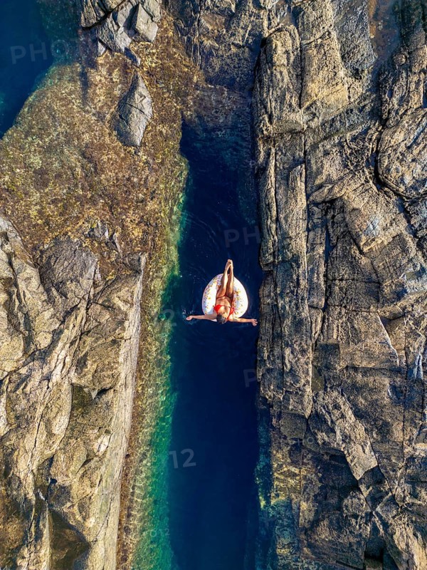 Top view of an unrecognizable woman relaxing on an inflatable float in a serene, narrow natural pool surrounded by rugged cliffs at Tindaya Beach, Fuerteventura