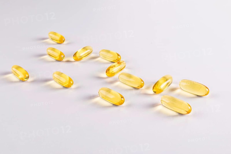 Close-up of omega 3 and vitamin E gel capsules on a white background. The glossy yellow capsules are scattered, highlighting their translucent texture and health benefits