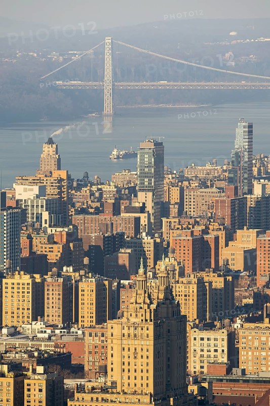 An aerial view captures the bustling landscape of New York City, highlighting the iconic George Washington Bridge in the background. The detailed cityscape showcases a mix of modern skyscrapers and classic architecture under the soft light