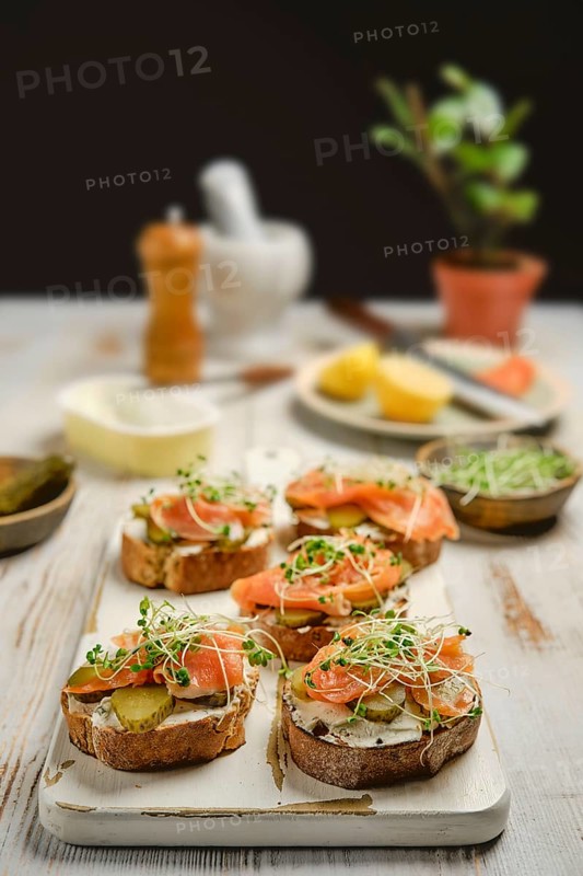 Freshly prepared open-faced sandwiches with smoked salmon, pickles, and watercress sprouts on crusty bread