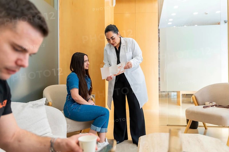 Professional doctor wearing a lab coat consulting a female patient in a modern aesthetic clinic waiting area, discussing treatment plans and providing detailed information about medical procedures