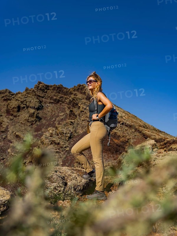 A female hiker stands in Timanfaya National Park, Lanzarote, surrounded by volcanic landscapes under a clear blue sky, embracing the park's rugged, natural beauty