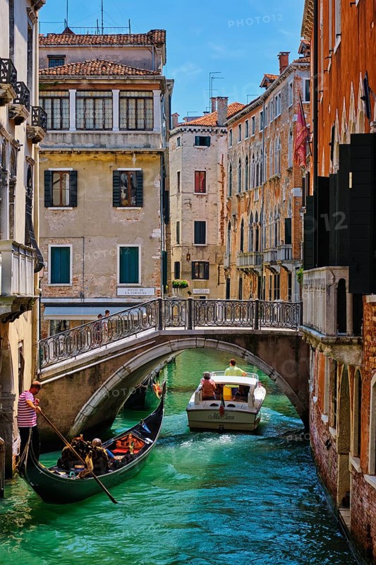 VENICE, ITALY, JULY 19, 2018: Narrow canal between colorful old houses with gondola boat with tourists and gonolier in Venice, Italy